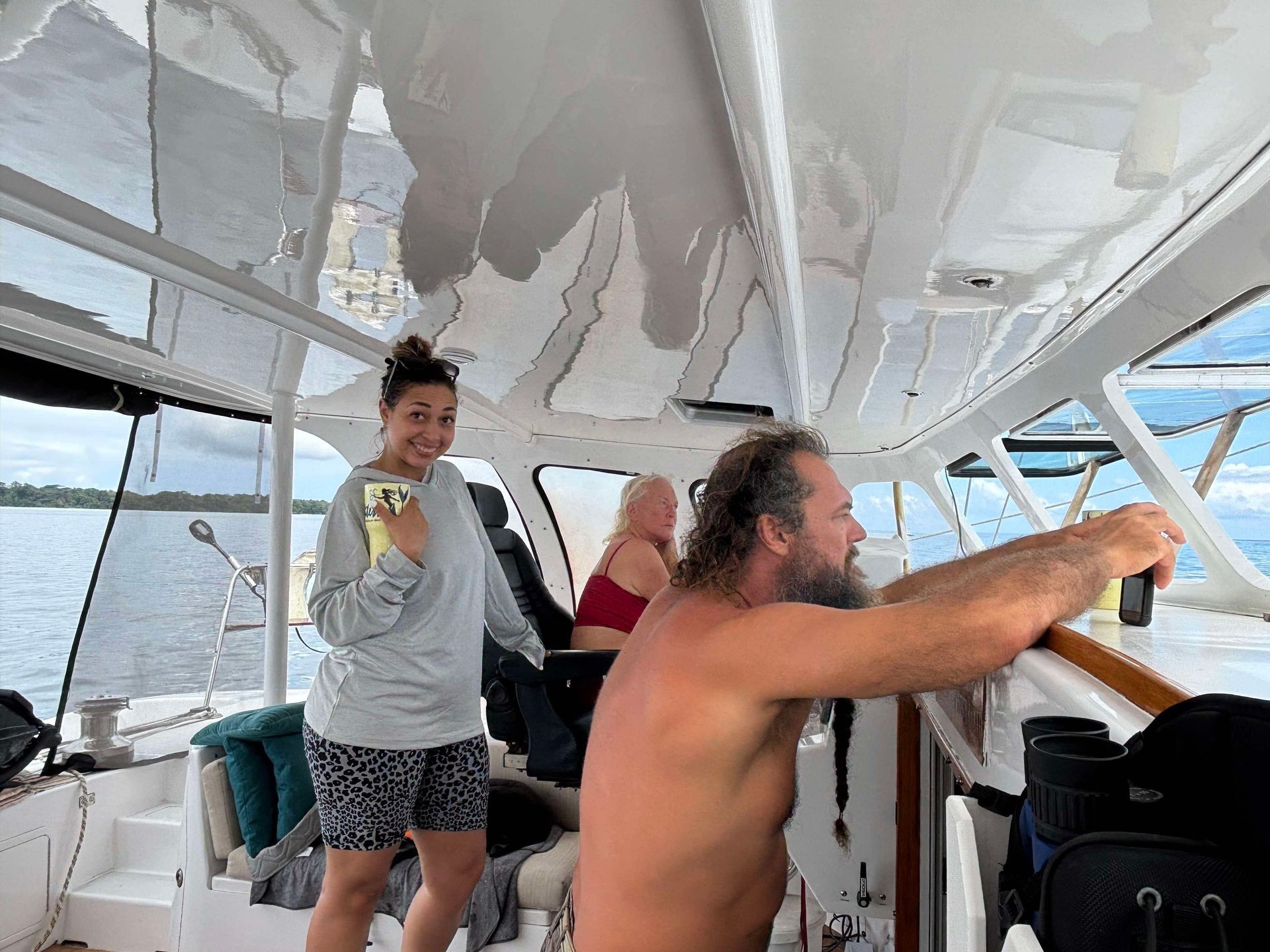 People sitting and standing inside a boat, with the ocean visible through the windows in the background.